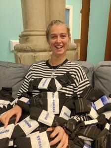 Charlotte smiling with hundreds of pairs of black socks on her lap