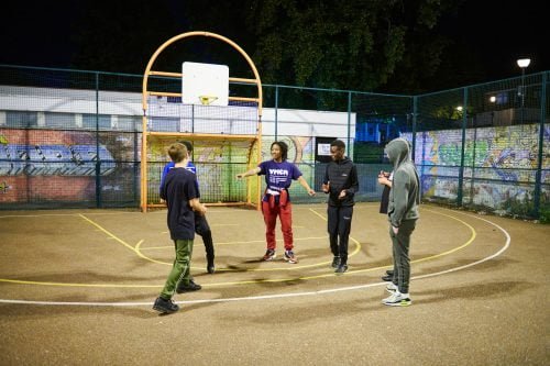 youth worker on a basketball court with a group of young boys smiling and talking