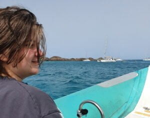 Sam sat on a boat with the sea behind him and a white boat in the distance