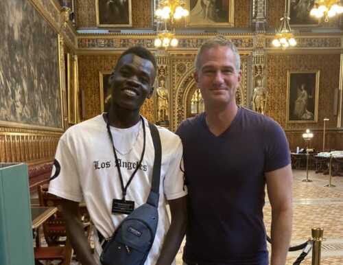 Nader stood next to Peter Kyle MP, both smiling wearing tshirts. They are stood in the houses of parliament in a grand room with golden walls.