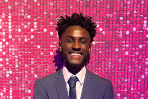 Adi smiling at the Youth Matters Awards with a pink glitter background