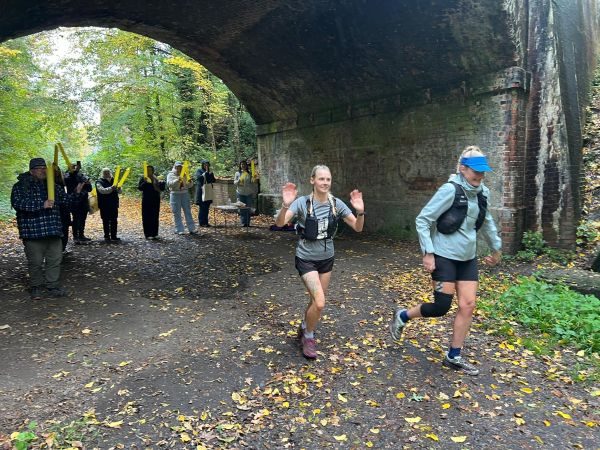 Leaving stop 2 surrey to sea run two female runners under an archway with supporters in the background