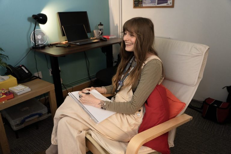A counsellor sits smiling and taking notes with a student in a session