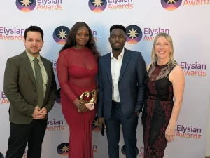 The group stand in front of the Elysian Awards branded background