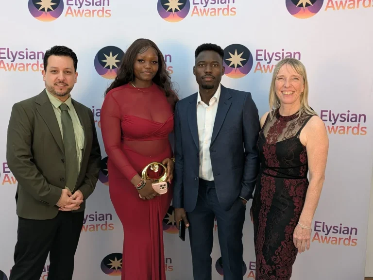 The group stand in front of the Elysian Awards branded background