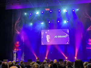 Distant shot of Jo Brand on stage, purple lighting