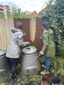 2 women seen from the back painting a fence by a waterbutt 