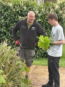 middle-aged man stood outside with a younger man holding a bushel of leaves