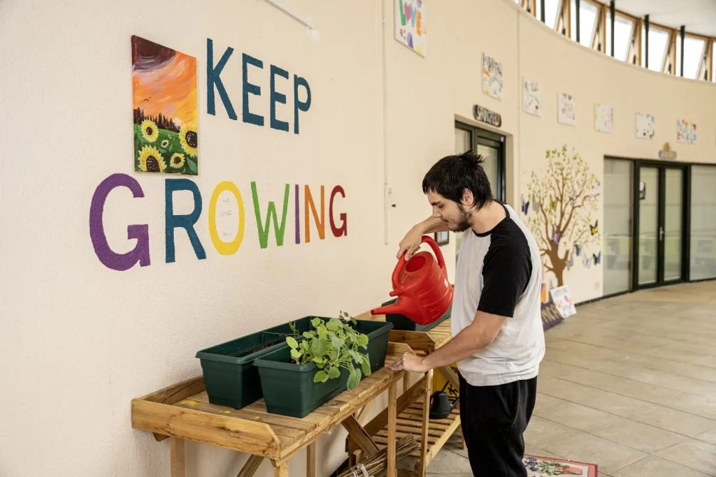 young man watering plants in front of a 'keep growing' mural