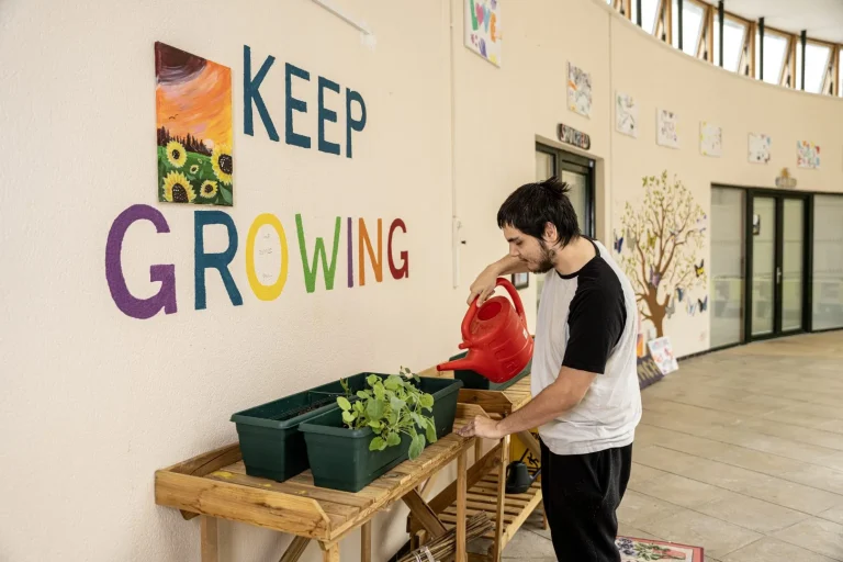 young man watering plants in front of a 'keep growing' mural