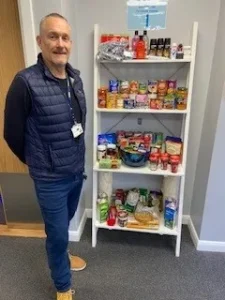 Man stood next to a shelf of food and toiletries