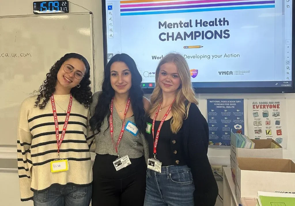 3 young women stood in front of a screen reading 'Mental Health CHAMPIONS'
