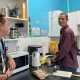 two men stood in a kitchen with one looking at the camera