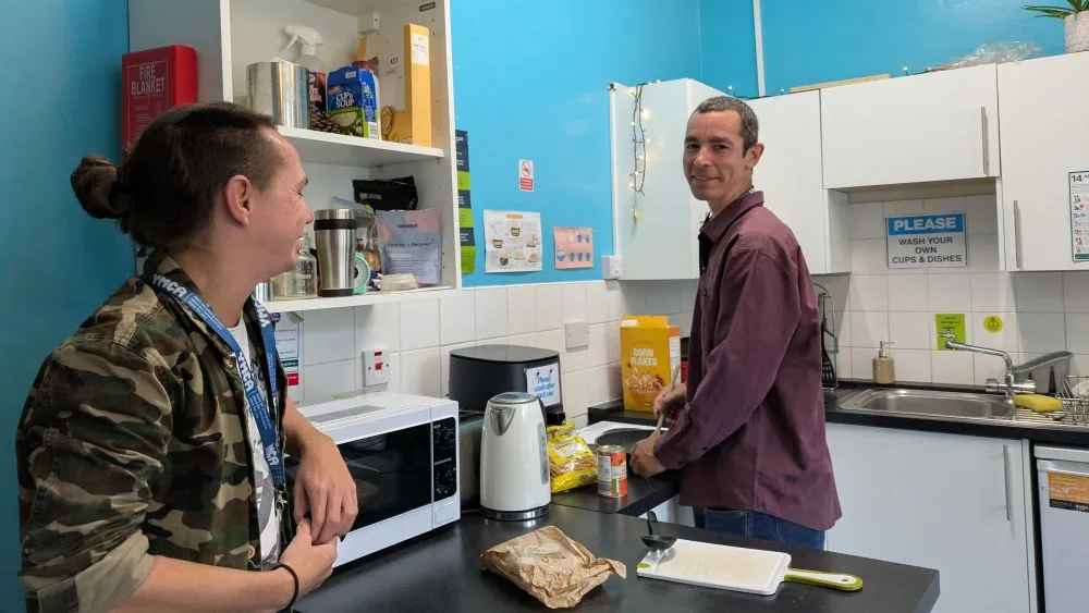 two men stood in a kitchen with one looking at the camera