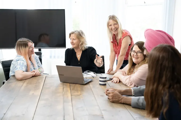 Six employees of YMCA DownsLink Group sitting around a table with a laptop