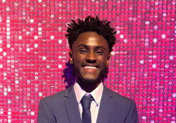 Adi smiling at the Youth Matters Awards with a pink glitter background
