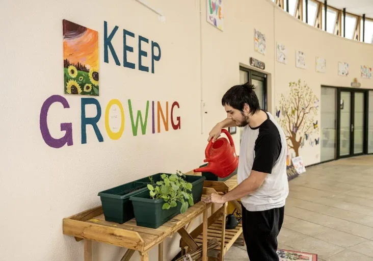 young man watering plants in front of a 'keep growing' mural