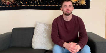 Best of Josh for article Josh sat on a sofa smiling, wearing a red jumper and blue jeans