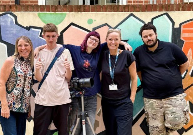 group of 5 people, men and women of various ages, standing in front of a wall with filming equipment