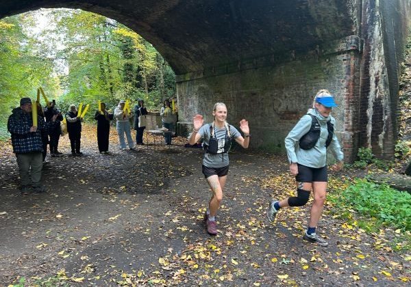 Leaving stop 2 surrey to sea run two female runners under an archway with supporters in the background