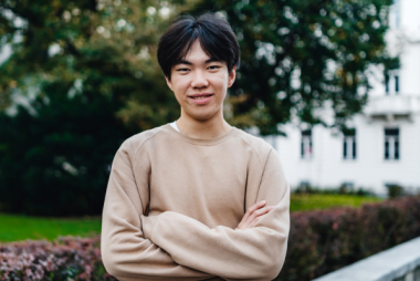 Image of Leo smiling with his arms crossed, wearing a beige jumper