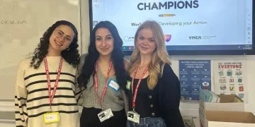 3 young women stood in front of a screen reading 'Mental Health CHAMPIONS'