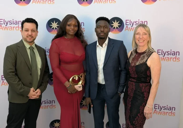 The group stand in front of the Elysian Awards branded background