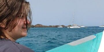 Sam Story Sam sat on a boat with the sea behind him and a white boat in the distance