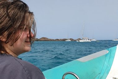 Sam sat on a boat with the sea behind him and a white boat in the distance