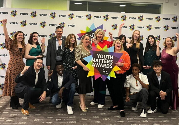Youth Matters Awards 2023, the whole of the YMCA DownsLink Group team smiling with their fists in the air holding a colourful 'Youth Matters' sign