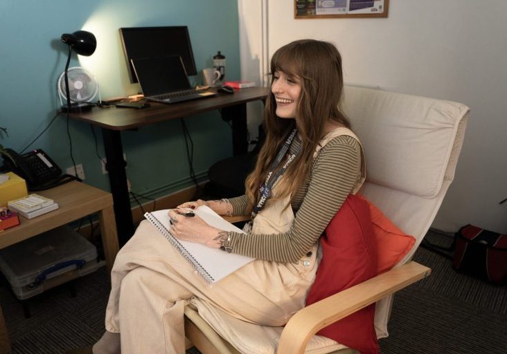 A counsellor sits smiling and taking notes with a student in a session
