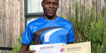 YMCA DownsLink Group_Guildford Foyer_Resident_Nader with certificate for banner image Nader stood in the garden in a blue sports tshirt holding up two certificates of achievement