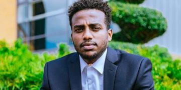 amanuel 2 for cover image Amanuel, a young man wearing a suit and white shirt with green bushes behind him