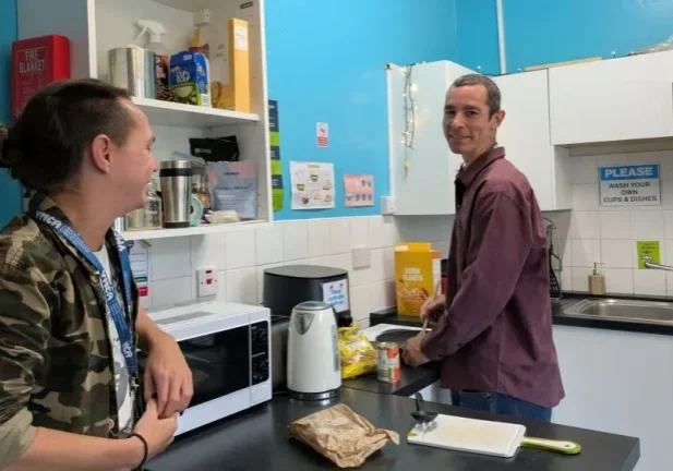 two men stood in a kitchen with one looking at the camera