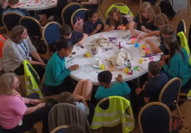 children and their teachers sat around a round table covered in crayons and papers